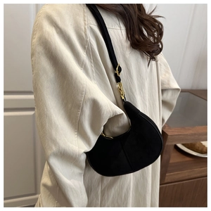 Side view of black suede crescent bag with gold metal buckle on female model