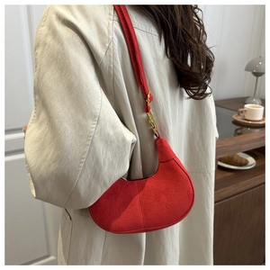 Detail of red suede crescent bag with gold hardware worn by a model in soft interior light