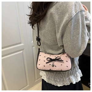 Pink seersucker shoulder bag with black bows and heart pendant detail on a model