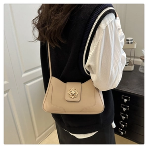 Detail view of khaki baguette bag with golden floral clasp shown on model's shoulder
