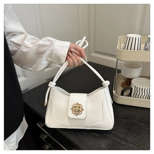 Detail of white leather handbag featuring a golden floral clasp and knotted handle decor