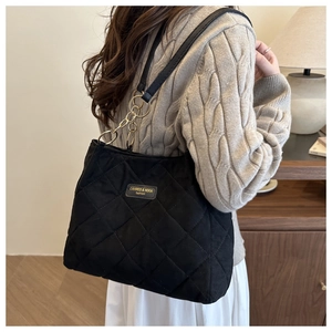 Detail of black quilted tote bag with gold chain strap and logo patch on model