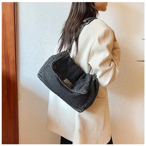 Detail einer grauen Denim-Umhängetasche mit Metallkette und Nieten auf dem Überschlag