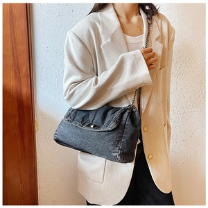 Nahaufnahme der schwarzen Denim-Umhängetasche mit Silberkette auf einem beigen Blazer