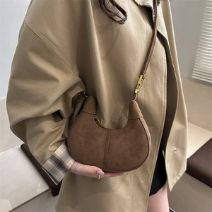 Minimalist brown suede crescent bag with gold hardware shown on person in trench coat