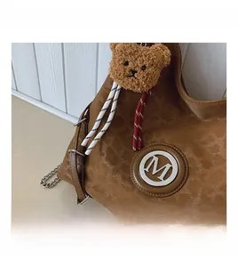 Close-up of brown textured shoulder bag with M logo and plush bear pendant detail