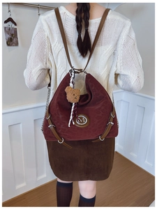 Close-up of burgundy retro backpack with metal M logo and plush bear charm detail