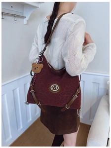 Detail of burgundy leopard print tote bag featuring a silver M logo and plush bear charm
