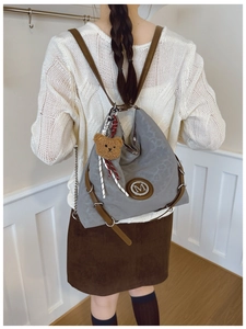 Detail of grey textured crossbody bag with brown leather straps and plush bear charm