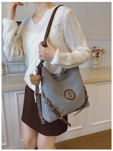 Detail of grey hobo bag with M logo, brown leather straps and plush bear charm