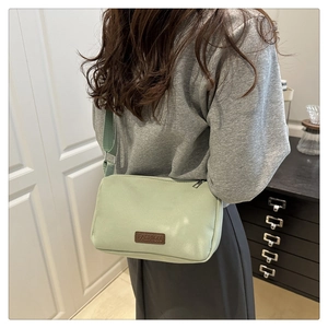 Détail du sac bandoulière en tissu vert clair avec écusson FASHION et zip argenté