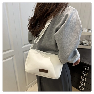 Détail d'un sac bandoulière en nylon blanc avec écusson en cuir et bandoulière réglable