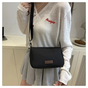 Gros plan d'un sac bandoulière noir en tissu avec patch cuir porté par un mannequin
