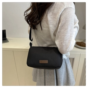 Détail d'un sac bandoulière en toile noire avec un patch en cuir marron sur un mannequin