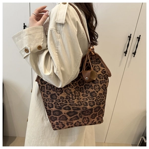Detail of a large leopard print tote bag with brown leather straps shown on shoulder