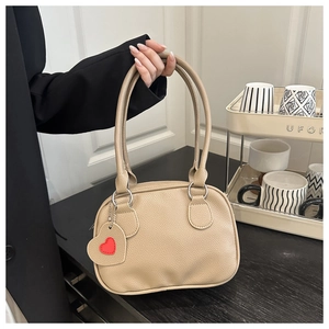 Dettaglio borsa in pelle martellata beige con anelli d'argento e ciondolo a cuore