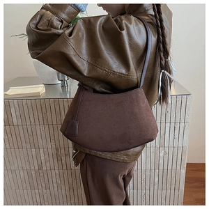 Détail du sac bandoulière demi-lune en daim marron foncé porté par un mannequin