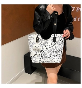 Close-up of white graffiti tote bag with plush cloud charm on a model's shoulder