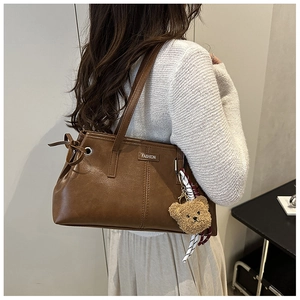 Detail of vintage brown leather shoulder bag with plush bear charm and ribbon