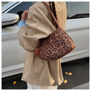 Détail du sac léopard sous le bras avec fine bandoulière marron et breloque en cuir