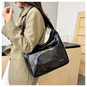 Detail view of large glossy black patent leather tote bag with gold fashion lettering