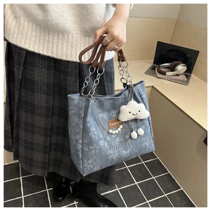 Détail d'un sac cabas en denim bleu à fleurs avec bandoulière chaîne et porte-clés