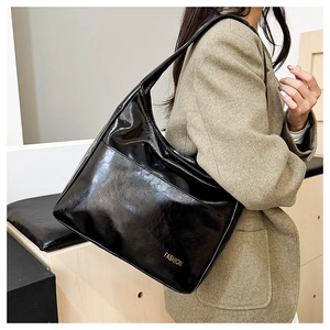 Close-up of black patent leather hobo bag with gold fashion lettering and wide strap