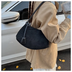 Détail du sac sous le bras en daim noir avec bandoulière nouée et pendentif carré