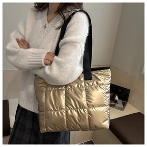Detailed view of a gold quilted tote bag with thick black straps on model's shoulder
