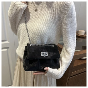 Detail of black velvet crossbody bag featuring a sparkling rhinestone buckle and silver chain