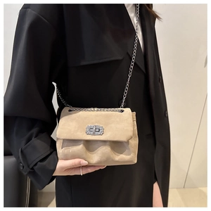 Detail of beige suede crossbody bag featuring rhinestone buckle and silver chain strap