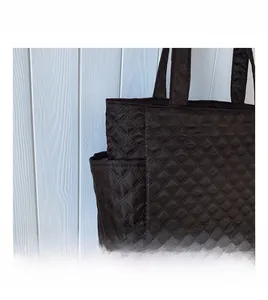 Detail of black quilted tote bag showing side pocket and nylon texture on white background