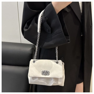 Detail of white pleated cloud bag with diamond buckle and silver chain on black blazer