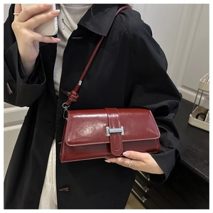 Detailed view of burgundy glossy leather shoulder bag with sleek silver hardware buckle