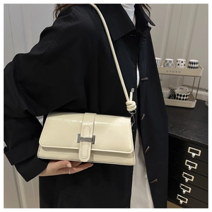 Detail of minimalist cream leather baguette bag with silver buckle worn on a black coat