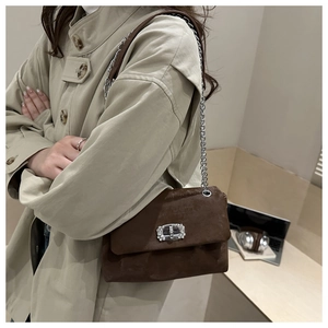 Detail of a brown suede shoulder bag featuring a silver chain and rhinestone buckle
