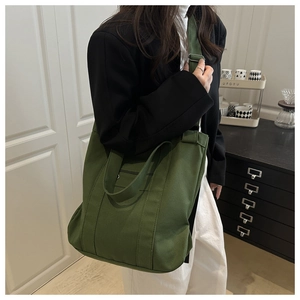 Détail du sac en toile vert foncé montrant la poche zippée avant et la bandoulière réglable
