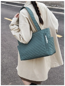 Outdoor shot of dark green quilted tote bag with side pockets and wide shoulder straps