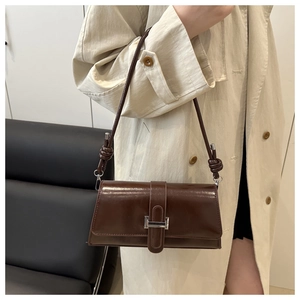 Detail of a dark brown baguette bag featuring unique knotted strap and silver metal buckle