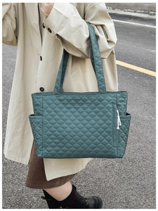 Detail of dark green quilted tote bag featuring a side pocket and white knot zipper pull