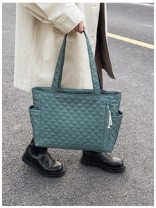 Detail of green quilted tote bag with side pocket and drawstring zipper on street