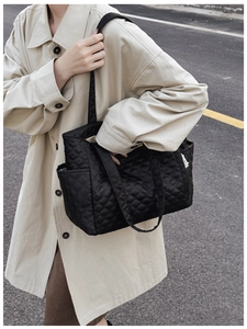 Detail of black quilted tote bag with diamond pattern and side pocket on female model
