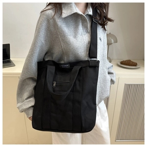 Détail du sac cabas en toile noire montrant la large bandoulière et la poche zippée
