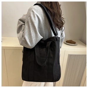 Detail of black canvas bucket bag with adjustable wide strap and white Fashion logo label