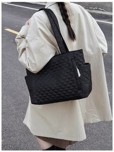 Black quilted tote bag with diamond pattern and side pocket shown in outdoor use