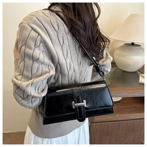 Détail d'un sac à bandoulière en cuir noir vintage avec boucle argentée porté par un modèle