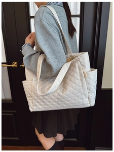 Detail of cream quilted tote bag featuring classic diamond stitching and wide shoulder straps