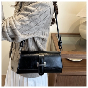 Detail of black glossy shoulder bag with silver buckle and knotted strap on model