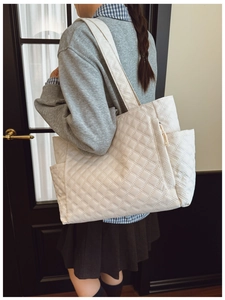 Detail of white quilted tote bag featuring a side pocket and padded shoulder strap
