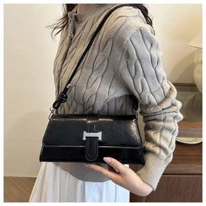 Detail of black glossy crossbody bag with silver buckle and knotted strap on model